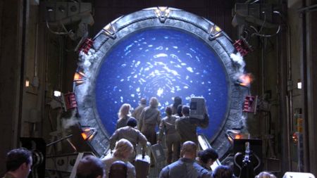 A group of people holding crates and walking through a Stargate during an episode of the TV show Stargate Atlantis.