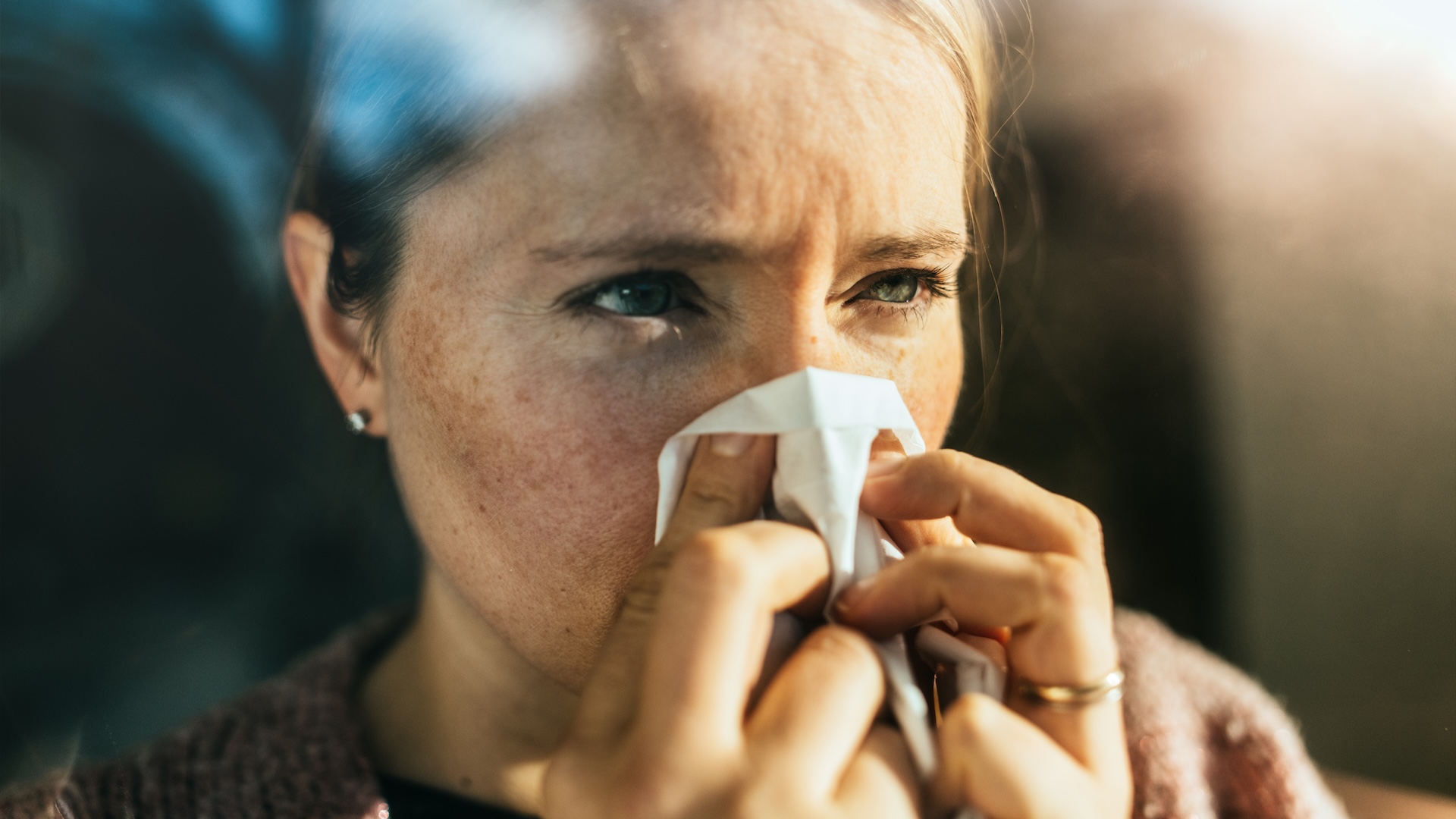 a woman sneezes into a tissue