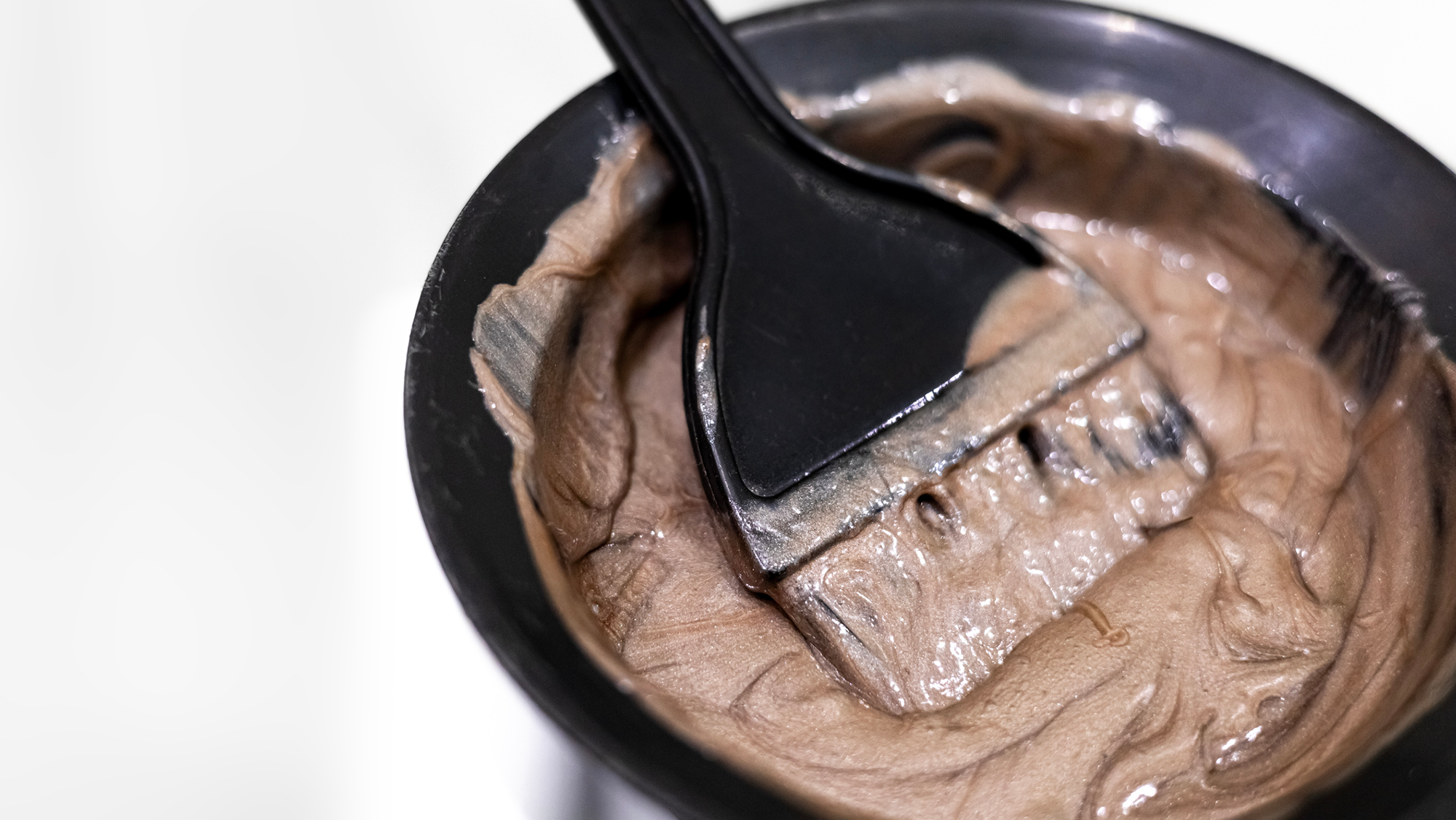 A close up of a paintbrush inside a bowl with brown hair dye in it.