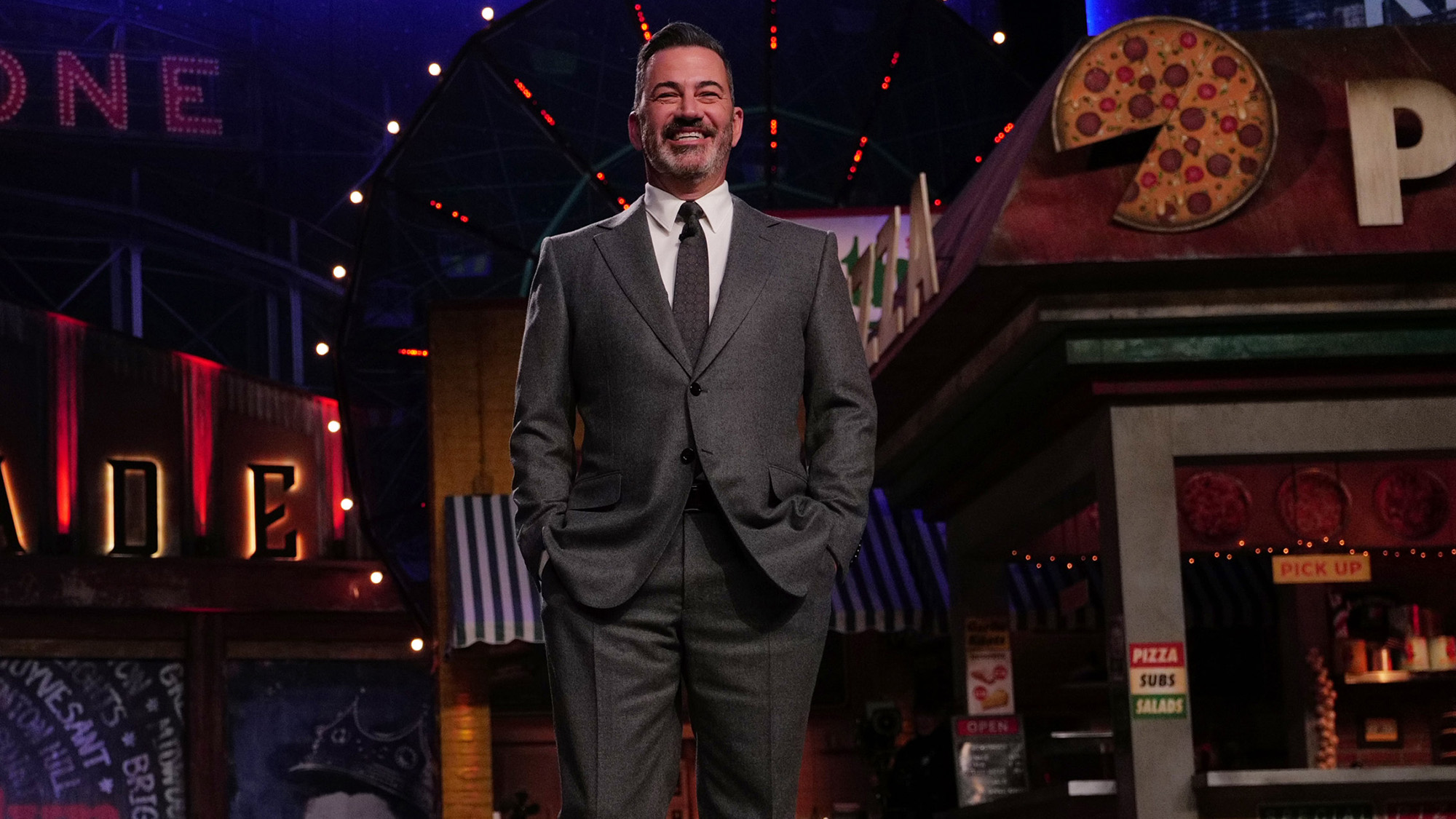 Jimmy Kimmel stands onstage in a grey suit smiling while filming Jimmy Kimmel Live! in Brooklyn. 