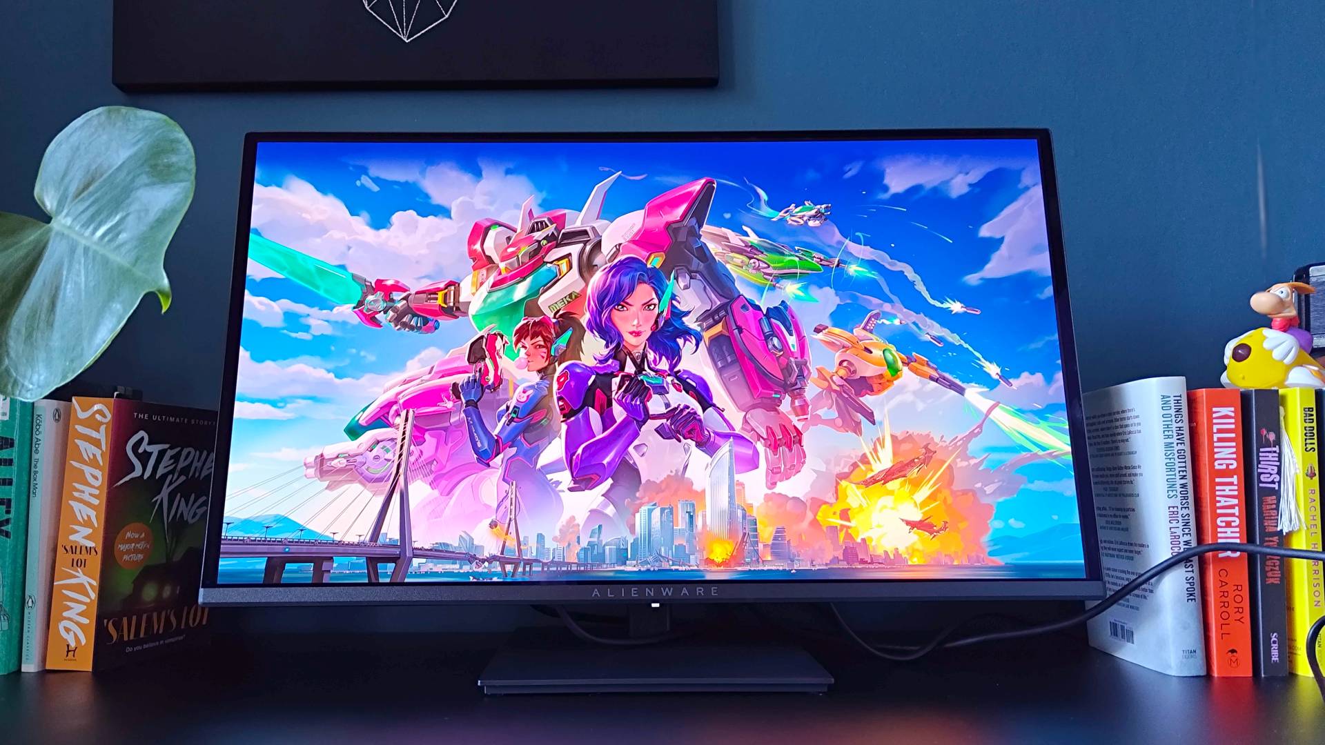 Alienware AW2726DM monitor on black desk with Overwatch loading screen displayed.