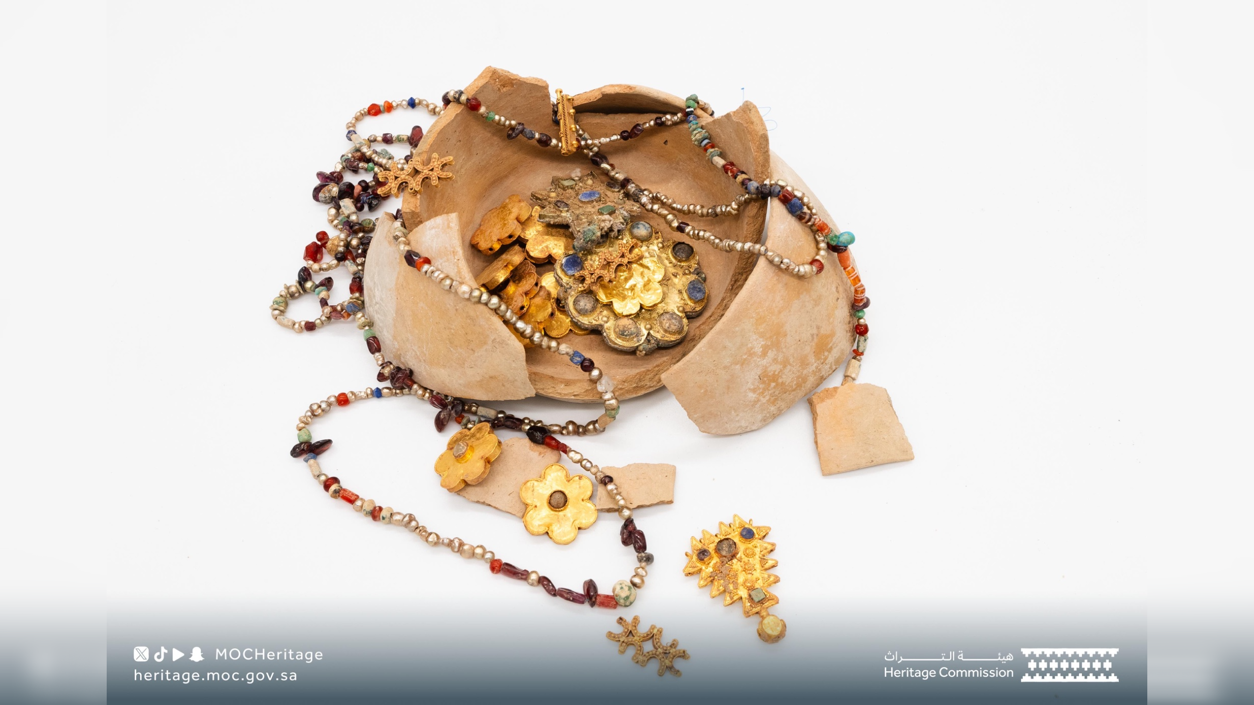 a broken ceramic pot with gold and beaded jewelry spilling out on a white background