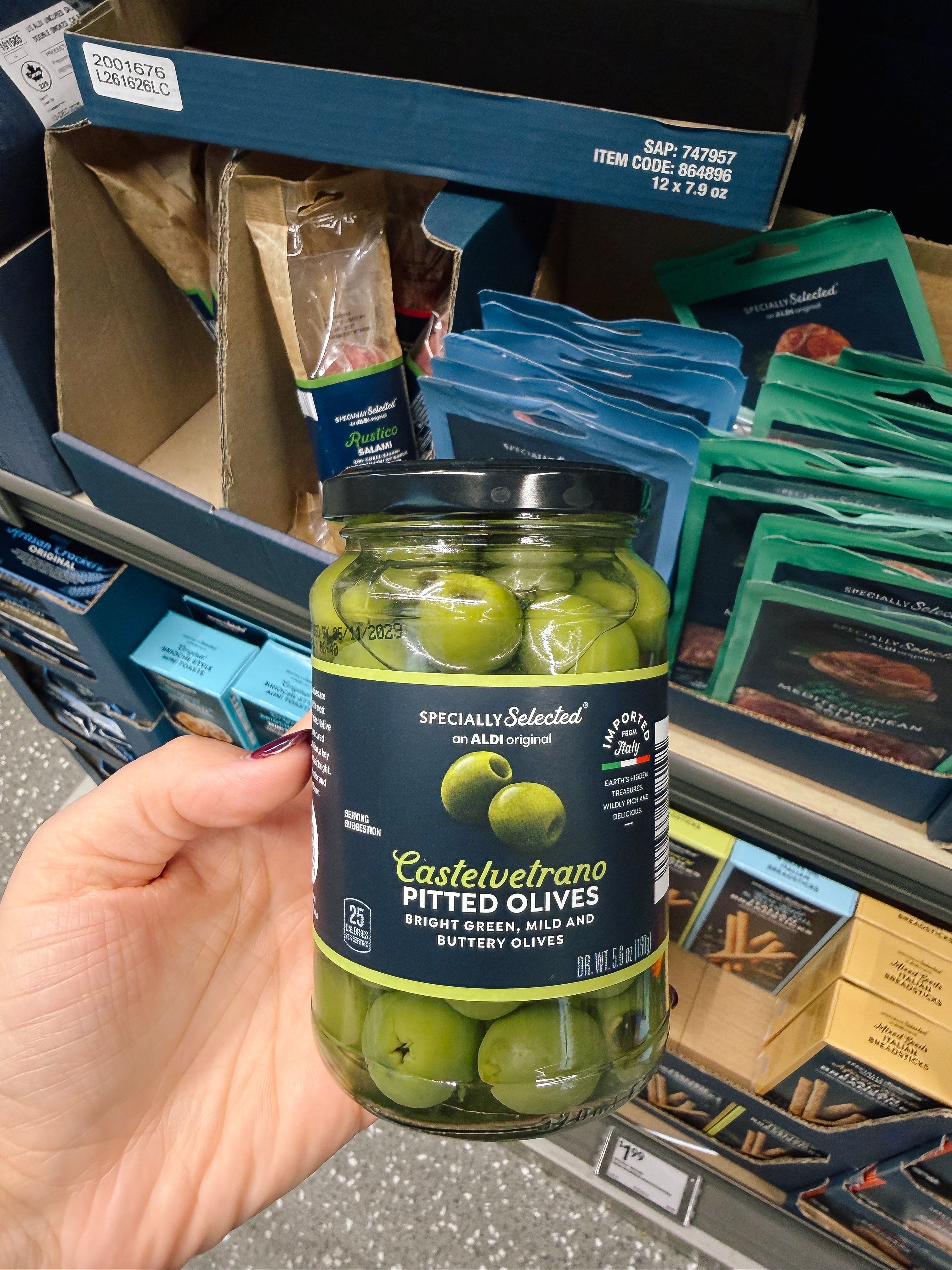 Person holding a jar of Castelvetrano pitted olives in a grocery store aisle