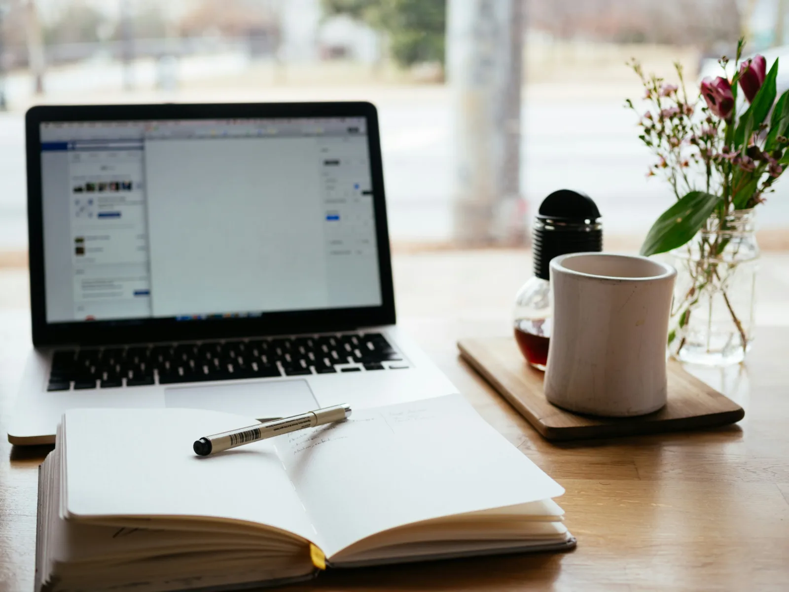 a notebook with a pen lying acorss it, a cup of coffee, and a laptop open to a word document. Everything someone needs to write a guest blog for Neon One!