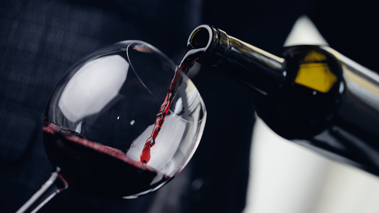 Pouring red wine from bottle into glass against black and white background